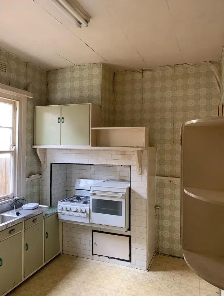 Retro kitchen with a gas stove built into a tile fireplace, white oven, and green cabinets under a window.