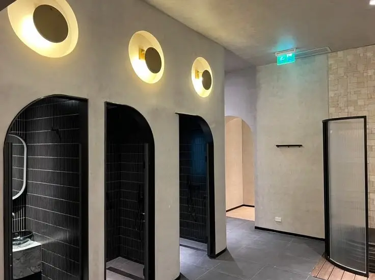 Three black-tiled arched stall entrances in a modern restroom with circular wall lights above each door